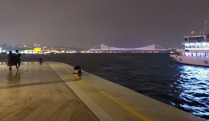 a pier with a lit up bridge in the distance and a boat on the water.