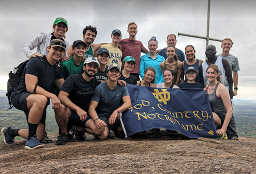 Group shot of Powerful Means holding a Notre Dame Flag in front of a cross on a mountain